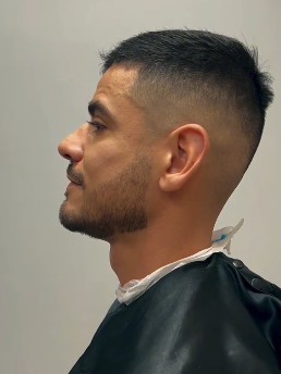Cliente de perfil com degradê alto e acabamento na barba