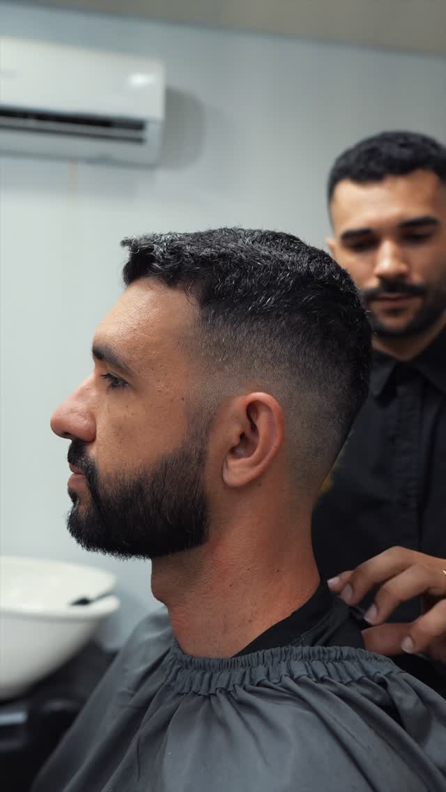 Cliente de perfil com o degradê pronto e o barbeiro ao fundo